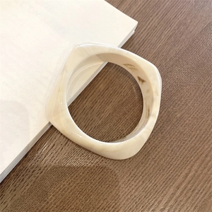 Close-up of cream resin square bangle with marble pattern over a book and wood table