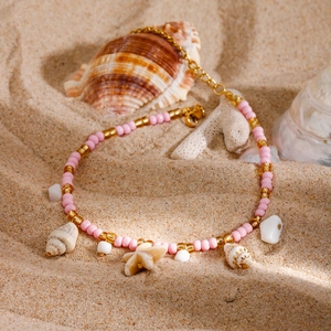 Pink and gold beaded anklet with natural shells and starfish on sandy beach background