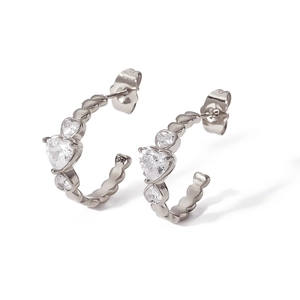 Vue macro de boucles d'oreilles C argentées avec zircone en cœur et détails de bordure perlé