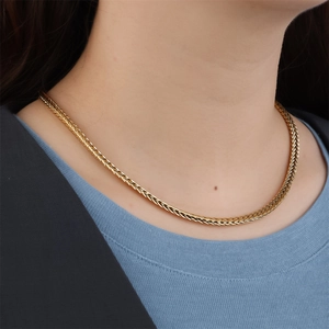 Close-up of golden woven snake chain necklace worn on neck with metallic texture detail