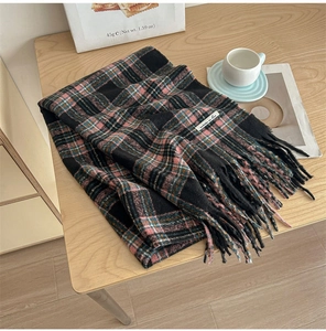 Close-up of red and green plaid scarf with long tassels on a cozy wooden table