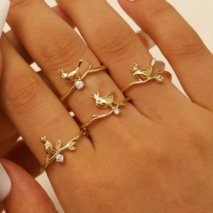 Detail of four golden rings featuring birds on branches with small zircon gemstone accents