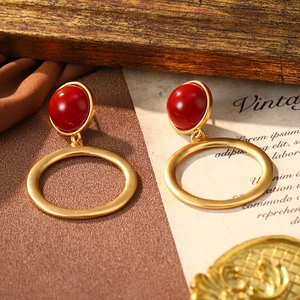 Close-up of vintage red enamel studs with golden open hoops on rustic script paper