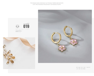 Detail of gold hoop earrings featuring pink five-petal flower pendants and zircon stones