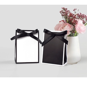 Détail de sacs cadeaux en papier blanc et noir avec nœuds en satin élégants et décor