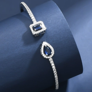 Detail of adjustable silver bangle featuring teardrop and emerald-cut blue gemstones