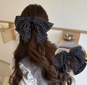 Détail d'une grande pince à cheveux à pois noirs portée sur de longs cheveux bouclés
