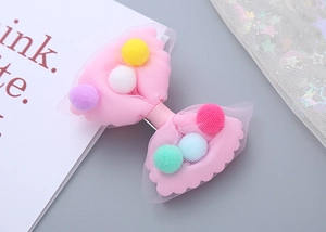 Detail of pink mesh bow hair clip with colorful pom-poms for girls over sparkling tulle