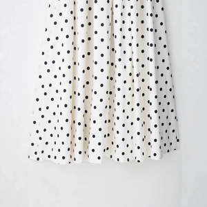Robe mi-longue blanche à pois avec tissu fluide présentée sur un fond minimaliste chic