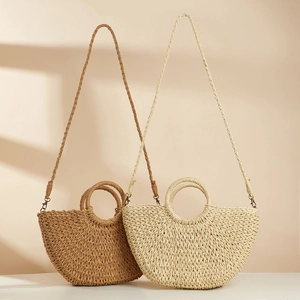 Detalle de bolsos de paja semicirculares en colores marrón y beige con asas redondas
