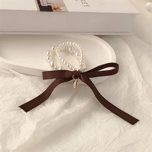Detail view of double-layered pearl hair tie with brown satin bow and gold charm