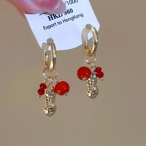 Detail view of gold peanut charm and red beads earring with price tag and elegant metal hoop
