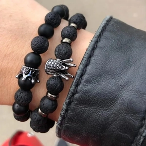 Detailed view of men's beaded bracelets with black lava stone and crown charm on wrist