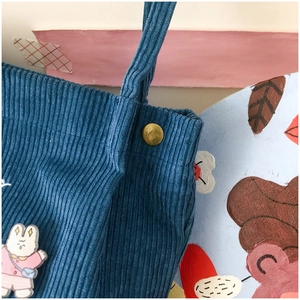 Detail of blue corduroy tote bag showing strap reinforcement and white rabbit brooch