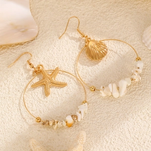 Macro detail of golden starfish and shell earrings on sand showing fine metal texture