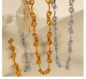 Detailed view of wave-shaped S-link gold and silver jewelry on a velvet display stand