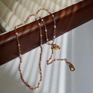 Detail of gold necklace chain with pink beads on a wooden jewelry box edge