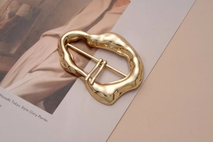 Detail of irregular molten-style gold metal buckle with dual pin for coat decoration