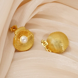 Detail of shell-shaped gold earrings with white pearl inlay on elegant silk fabric