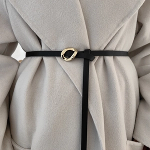 Close-up of a slim black leather belt with an irregular gold metal buckle on a beige coat