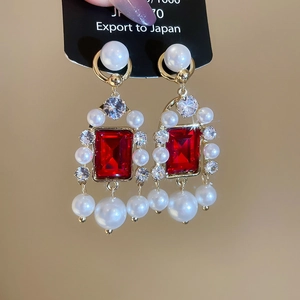 Vue détaillée des boucles d'oreilles dorées avec pierre rouge et perles blanches