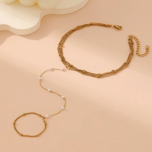 Detail of layered gold bracelet with white pearls and ring chain on pink background