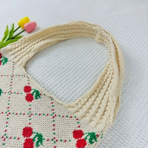 Detailed knit texture of beige cherry tote bag with red leaf pattern and grid design