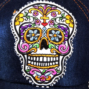 Macro detail of skull embroidery and rhinestones on dark blue denim baseball cap