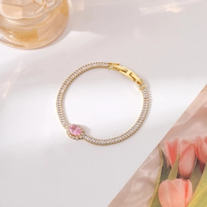 Close-up of golden bracelet featuring a pink oval gemstone and rectangular zircons