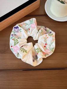 Detail of cream satin scrunchie with floral embroidery on wooden tea tray