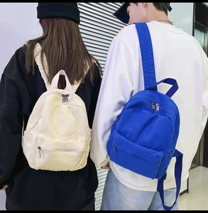 Detailansicht von Mini-Canvas-Rucksäcken in Creme und Blau, getragen von einem Model im Raum