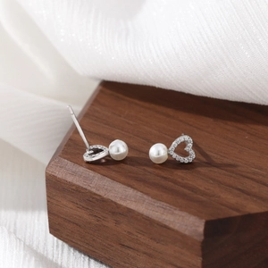 Elegant heart-shaped pearl earrings with small diamonds on a dark wooden surface