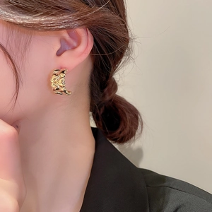 Detailed view of irregular lava texture gold earrings on a model wearing a black blazer