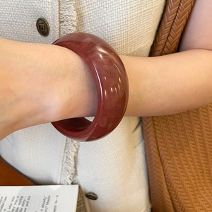 Close-up of a wide dark red resin bangle with smooth texture on a tweed background