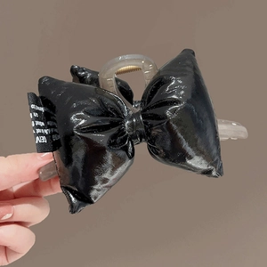 Handheld black glossy bow hair claw clip with semi-transparent grey base on brown backdrop