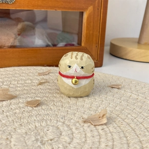 Close-up of hand-carved wooden cat figurine with orange stripes and gold bell on a mat