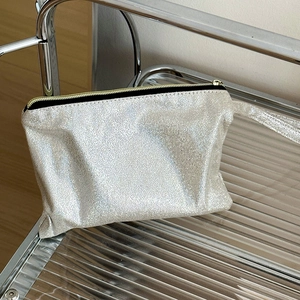 Macro shot of silver glitter makeup bag on glass shelf with black zipper detail