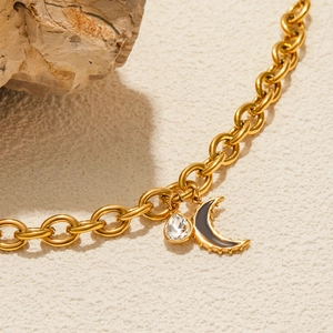 Close-up of gold moon and zircon droplet charms on a stainless steel watchband bracelet