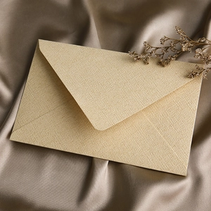 Elegant cream linen textured paper envelope displayed on champagne silk fabric background