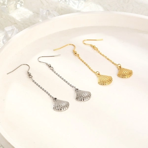 Detailed close-up of gold and silver seashell tassel earrings on a white ceramic tray
