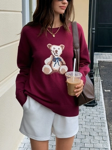 Close-up of wine red knitted sweater featuring a large teddy bear pattern for casual wear