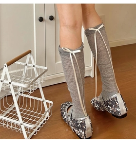 Detail of grey balletcore knit leg warmers with white ribbon bows and silver sequin shoes