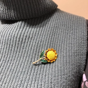 Fashionable enamel sunflower brooch with yellow petals and crystals on a grey sweater