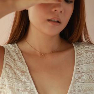 Close-up of golden bow-shaped pendant necklace worn by a model on a soft background
