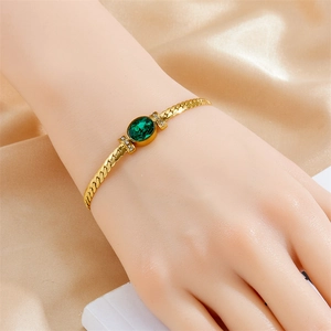 Gold chain bracelet with oval green gemstone and sparkling zircons on silk background