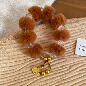 Gros plan du bracelet en perles avec pompon marron et pendentif floral doré