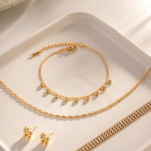 Golden titanium steel jewelry set with sparkling diamond pendants on white plate