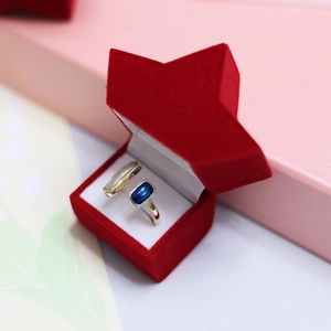 Golden open ring with blue rectangular gemstone in a red star-shaped velvet jewelry box