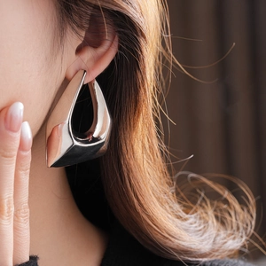 Close-up of minimalist silver triangular earrings worn by a model in a modern style