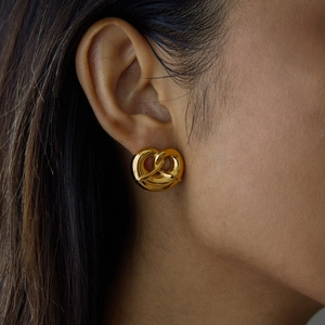 Close-up of a gold twist knot heart earring on a model, featuring polished steel finish